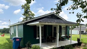 Een gelijkvloers huis met een veranda, een schommelstoel en een afvalbak.