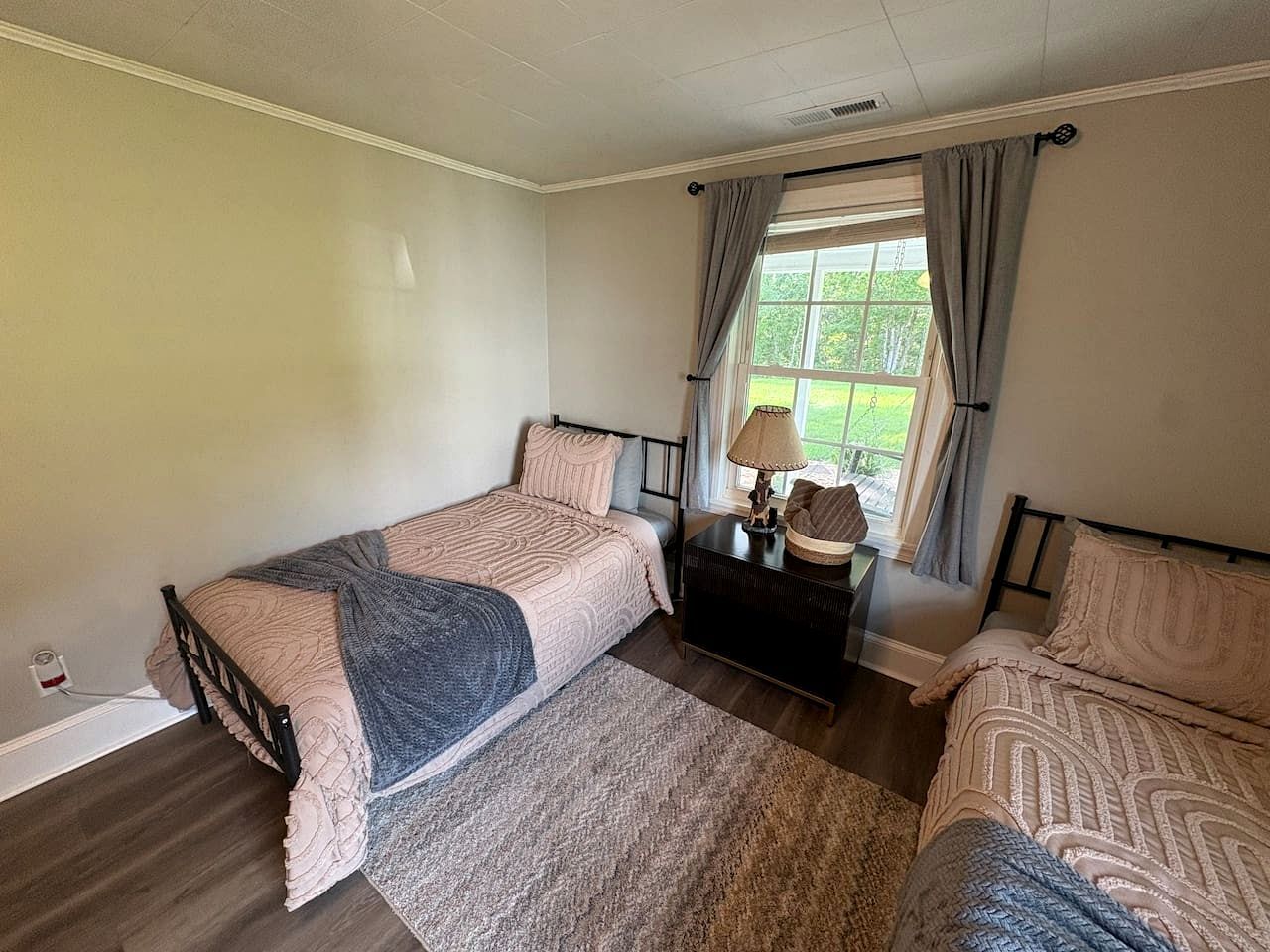 A bedroom with two beds, a nightstand, and a window with curtains.