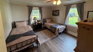 Slaapkamer met twee bedden, een plafondventilator, een raam met gordijnen en een houten dressoir.