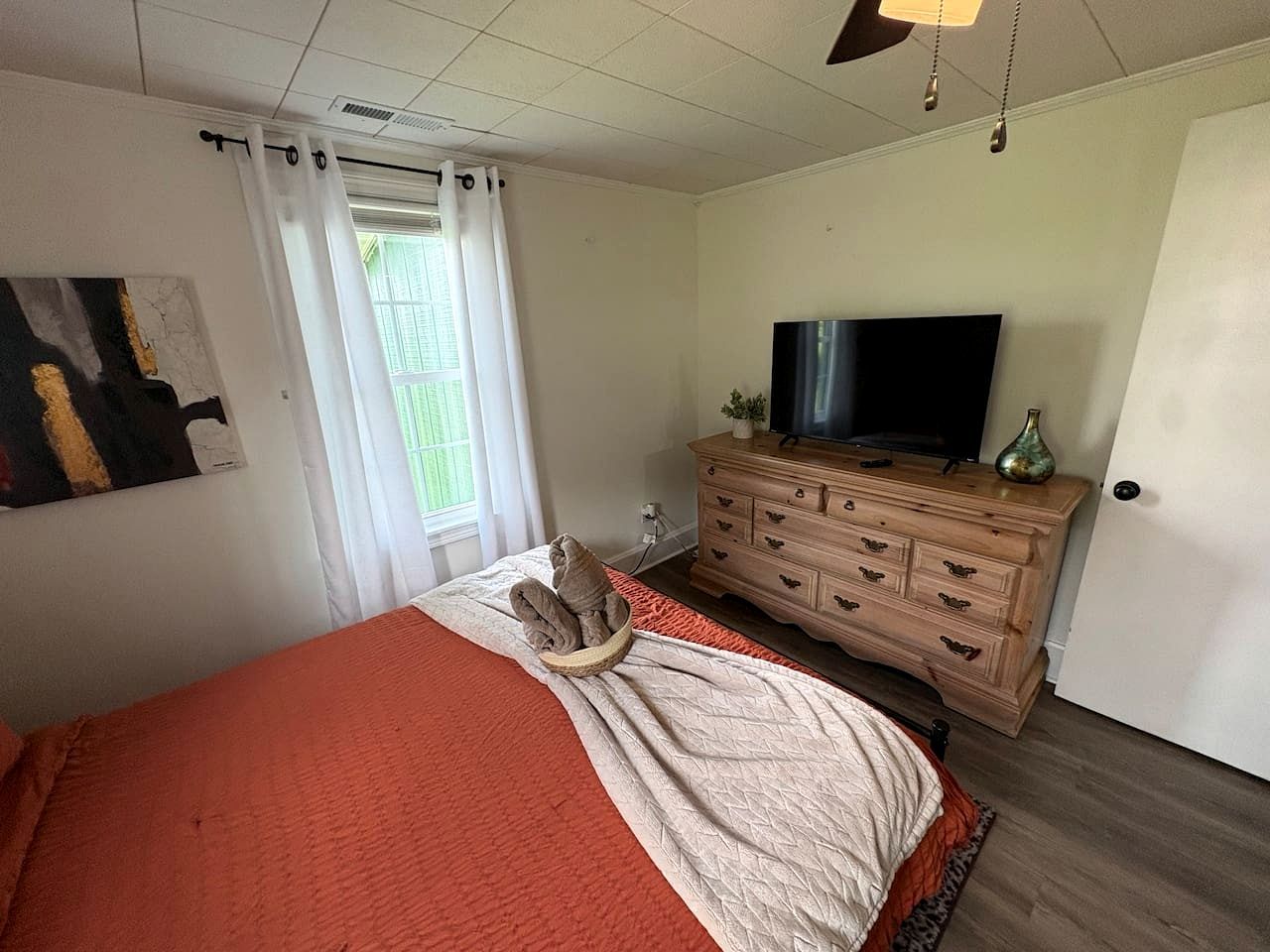 Quarto com cama, televisão, cómoda e janela com cortinas.