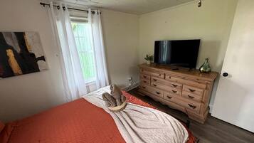 Quarto com cama, televisão, cómoda e janela com cortinas.