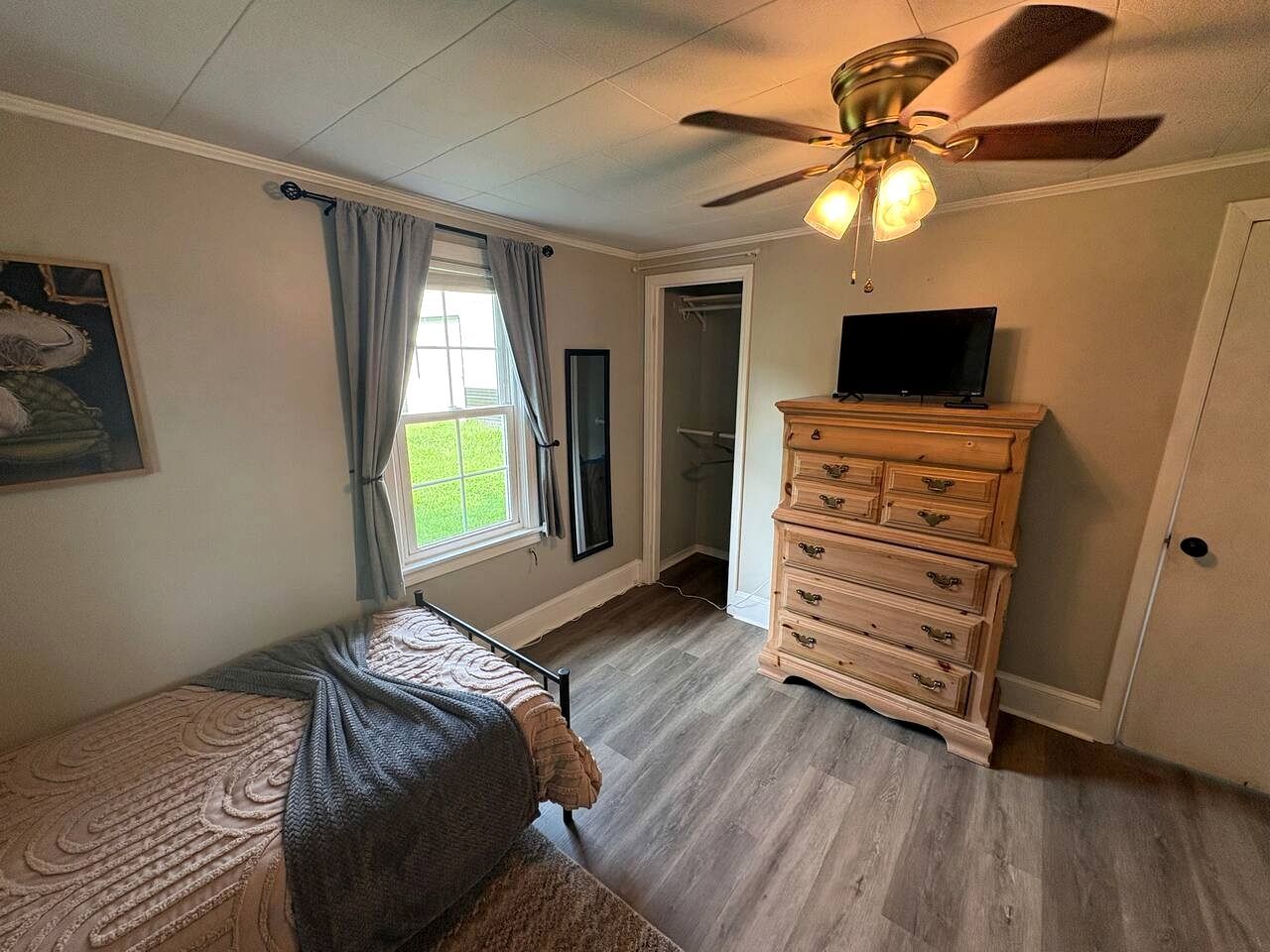 Un dormitorio con cama, cómoda, ventilador de techo y ventana con cortinas.