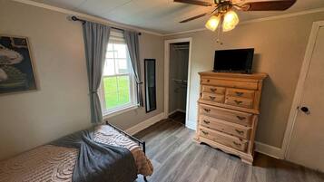 Un dormitorio con cama, cómoda, ventilador de techo y ventana con cortinas.