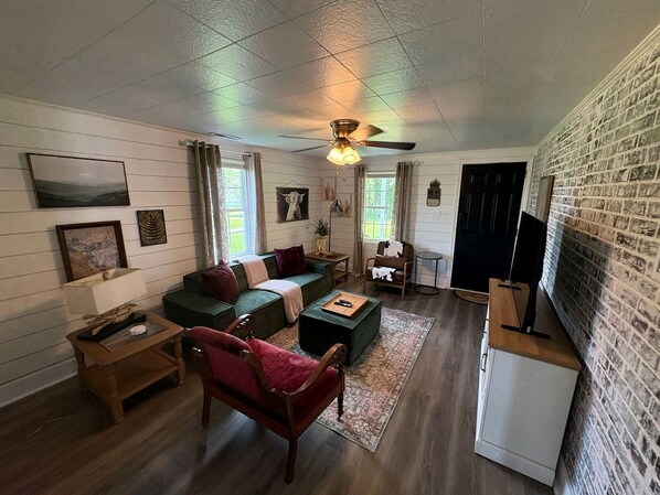 A cozy living room with a green sofa, a red armchair, a wooden coffee table, and a television on a stand.