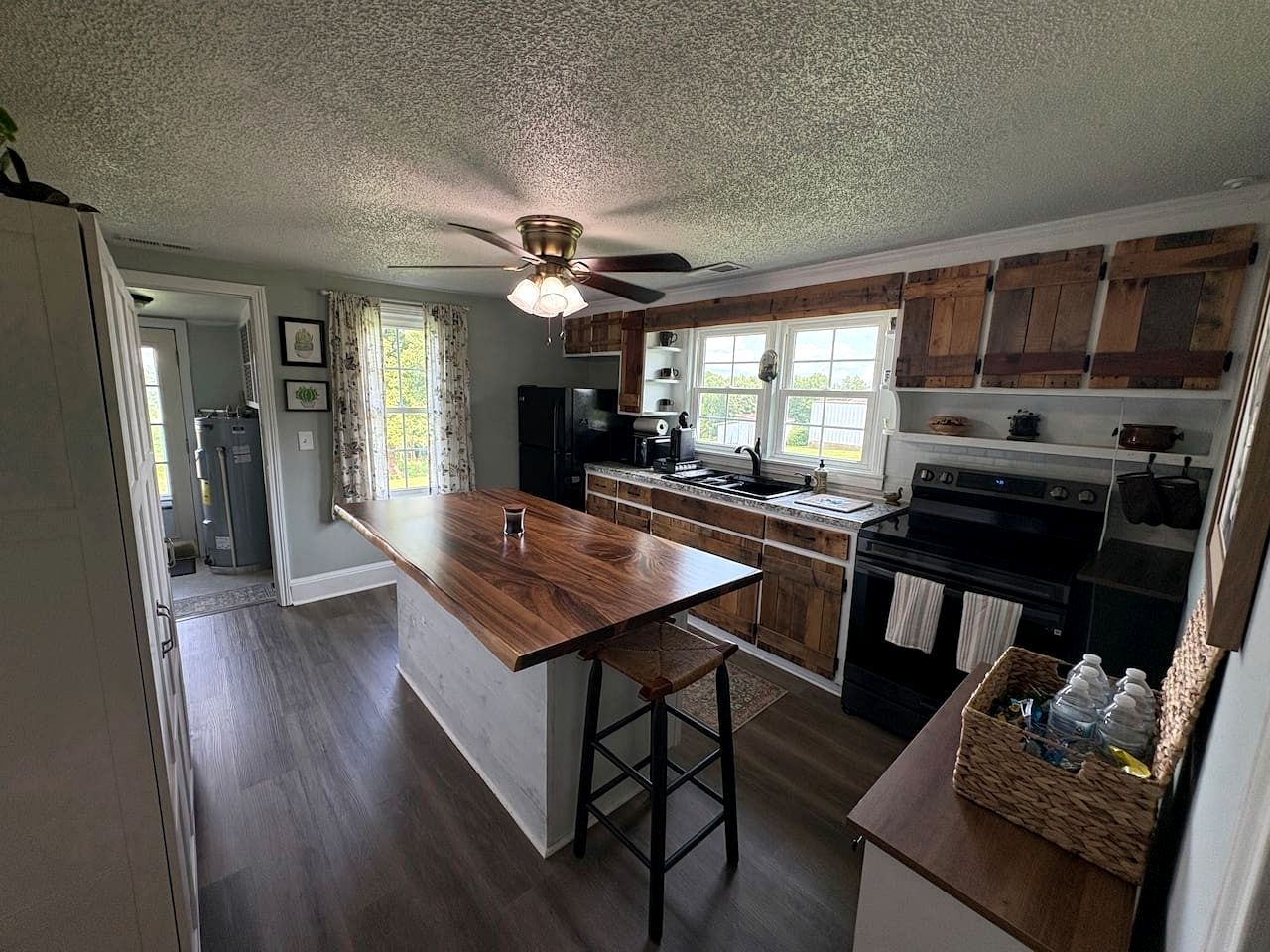 A kitchen with wooden cabinets, a central island, a ceiling fan, and a window with curtains.