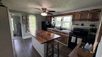 A kitchen with wooden cabinets, a central island, a ceiling fan, and a window with curtains.