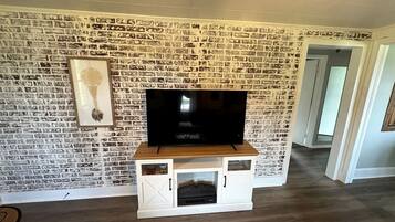 Un salon avec un mur décoré d’un motif en briques, un téléviseur à écran plat posé sur un meuble en bois et un meuble de rangement blanc doté de tiroirs.