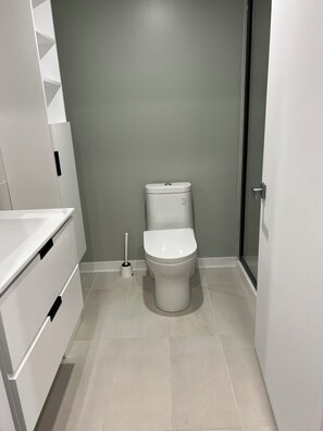 A modern bathroom with a toilet, a white sink, and a toilet brush. - Modern Studio Montréal - Heart of Downtown (Montréal)