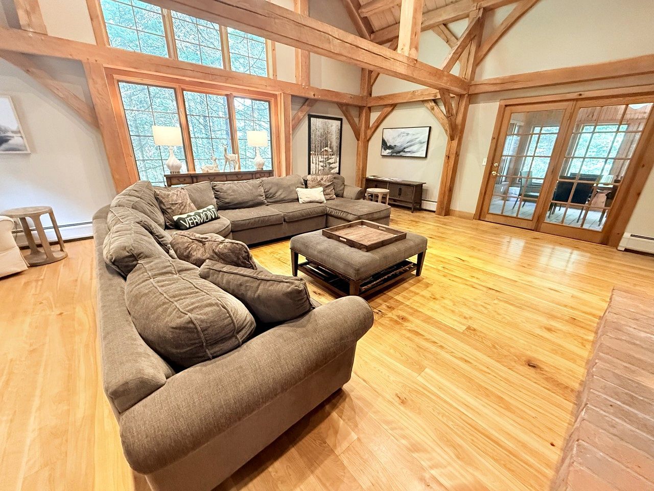 A spacious living room with a large sectional sofa, wooden flooring, and large windows.