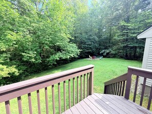 A wooden deck with a view of a well-maintained lawn and dense trees in the background. - Mountain Retreat with Stone Fireplace & Game Room Near Stratton, Magic Mountain & Bromley Mountain, Peru, Vermont (Peru)