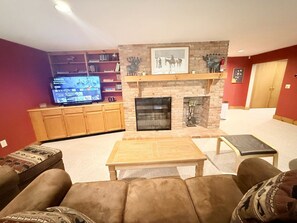 A living room with a fireplace, a television, and a bookshelf. - Mountain Retreat with Stone Fireplace & Game Room Near Stratton, Magic Mountain & Bromley Mountain, Peru, Vermont (Peru)