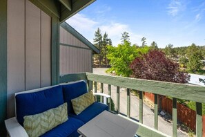 A balcony with a blue sofa and a small table, overlooking a road and greenery. - Lakeside Vibes | 2BR, Walk to Boulder Bay, Pool (Big Bear Lake)