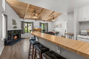 A modern kitchen with a central island, wooden ceiling beams, a fireplace, and a dining area with a view. - Lakeside Vibes | 2BR, Walk to Boulder Bay, Pool (Big Bear Lake)