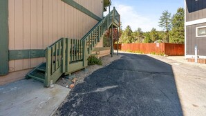 A building with a green staircase leading to a door, a paved driveway, and a wooden fence in the background. - Lakeside Vibes | 2BR, Walk to Boulder Bay, Pool (Big Bear Lake)