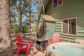 Une terrasse en bois avec un jacuzzi, deux fauteuils Adirondack et un espace abrité.