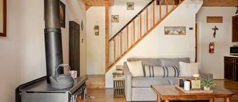 A cozy living room with a fireplace, a sofa, a coffee table, and a staircase.