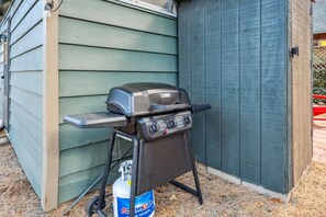 Ein tragbarer Grill mit Gasflasche, aufgestellt an einem Gebäude mit Verkleidung.