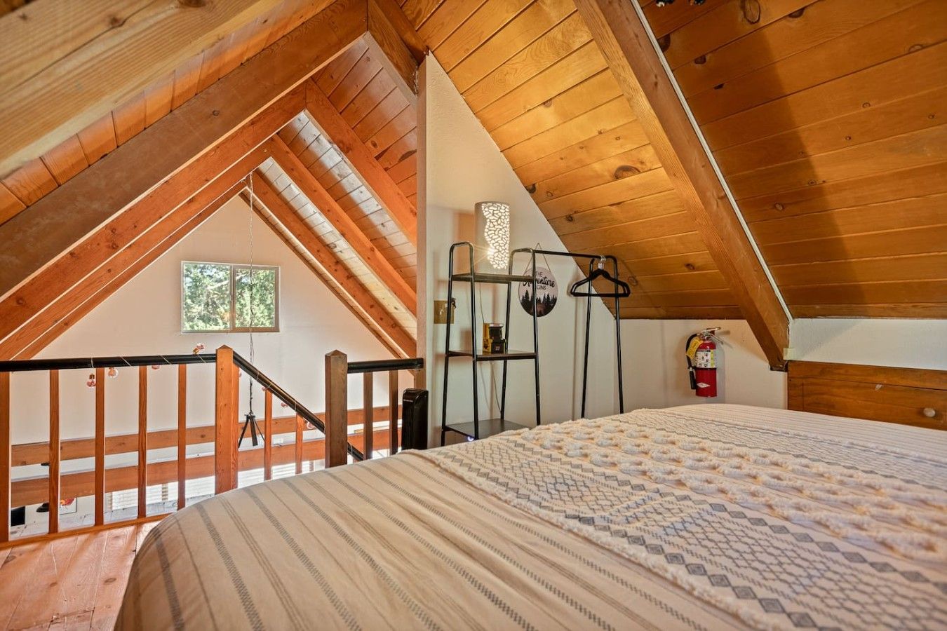 Une chambre avec un plafond en pente, un lit recouvert d’une couvre-lit à motifs, une fenêtre et un extincteur.