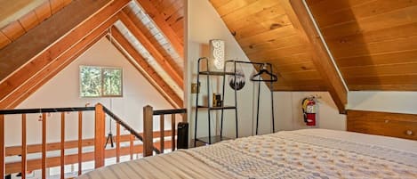 A bedroom with a sloped ceiling, a bed with a patterned bedspread, a window, and a fire extinguisher.