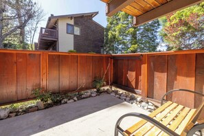 A wooden deck with a metal bench, surrounded by a wooden fence, and a house in the background. - Après All Day | Walk to Summit, Community Hot Tub (Big Bear Lake)