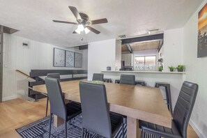 A dining area with a wooden table, black chairs, a ceiling fan, and a kitchen in the background. - Après All Day | Walk to Summit, Community Hot Tub (Big Bear Lake)