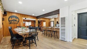 Un comedor con una mesa y sillas de madera, una cocina al fondo y una puerta a la derecha.