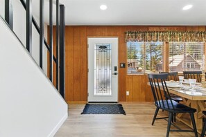 A dining area with a wooden table and chairs, a glass door with a frosted pattern, and a view of the outside through a window with blinds. - Big Bear Cabana Near Lake W/ Hot Tub, Shuffleboard (Big Bear Lake)
