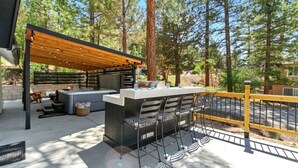 Un patio al aire libre con una parrilla empotrada, zona de estar y una pérgola con luces colgantes.