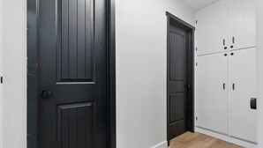 Un pasillo con dos puertas negras y varios armarios blancos.
