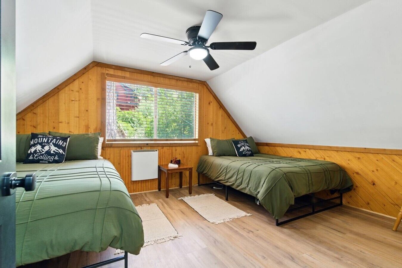 Ein kleines, gemütliches Schlafzimmer im Dachgeschoss mit zwei Betten, einem Deckenventilator, einem Fenster mit Jalousien und einer Heizung.