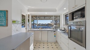 A modern kitchen with a view of a body of water, equipped with a dishwasher, a coffee machine, and a stove. - 4 Murray Avenue, Forster (Forster)