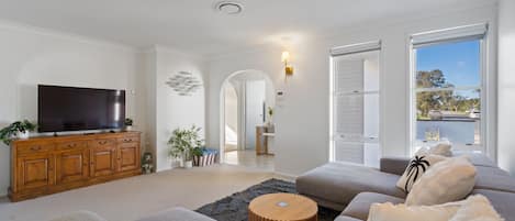 Una sala moderna con televisor de pantalla plana, aparador de madera, sofás grises y vistas al exterior.