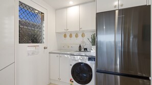 A compact kitchen with a stainless steel refrigerator, a washing machine, and a sink. - 4 Murray Avenue, Forster (Forster)