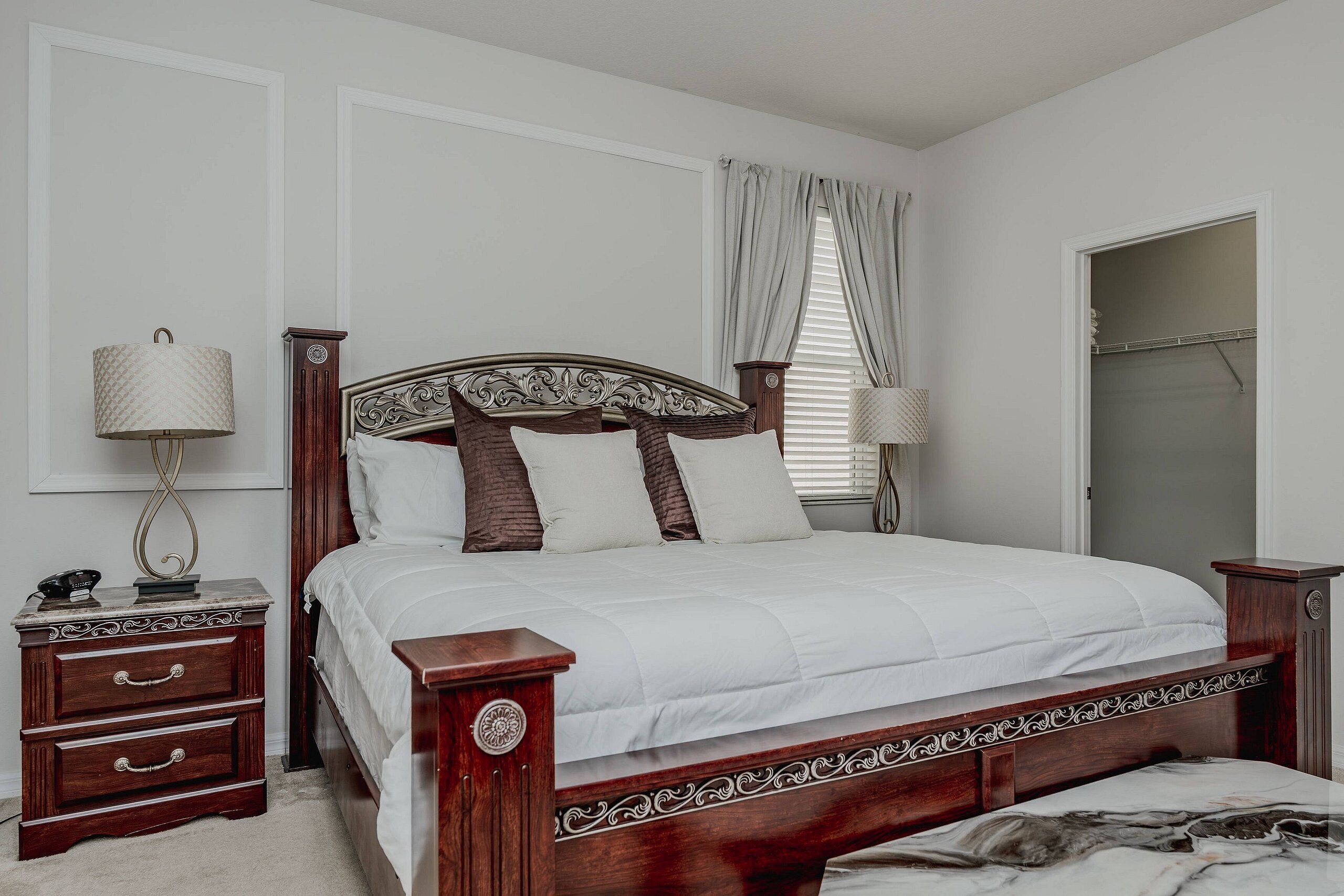 Une chambre à coucher avec un lit en bois, une table de chevet avec une lampe, une commode et une fenêtre avec des rideaux.