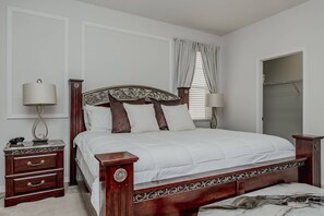 A bedroom with a wooden bed, a nightstand with a lamp, a dresser, and a window with curtains. - 5BR Veranda Palms Home Near Disney for 14 (Kissimmee)
