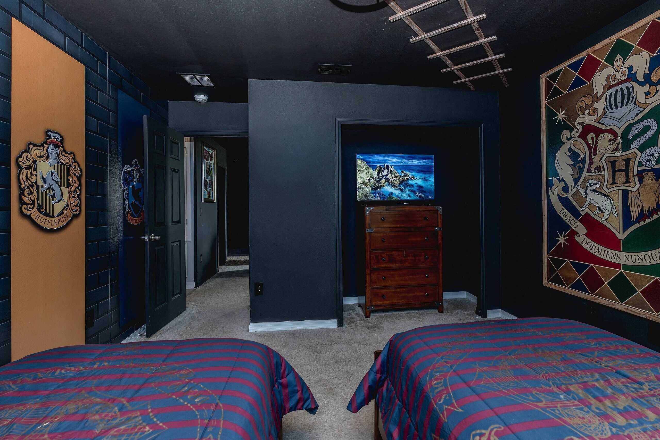 Ein Zimmer mit zwei Betten, einem Schminktisch, einem Fernseher und einer Wand mit einem Wappen.