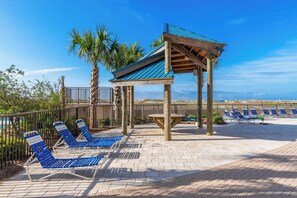 Un espace de détente aménagé sur la plage, avec des chaises longues bleues et une structure de pergola en bois.
