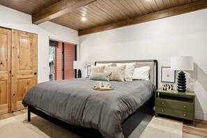 Un dormitorio con cama, mesitas de noche, una puerta de madera y una ventana.