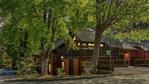 A two-story building with a balcony, a parking lot, and trees in the foreground. - Slope & Cedar House | Hot tub, Steps 2 Snow Summit (Big Bear Lake)