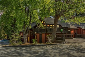 A two-story building with a balcony, a parking lot, and trees in the foreground. - Slope & Cedar House | Hot tub, Steps 2 Snow Summit (Big Bear Lake)