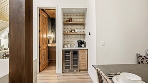 A compact kitchen with a microwave, coffee maker, and shelves with kitchenware. - Slope & Cedar House | Hot tub, Steps 2 Snow Summit (Big Bear Lake)