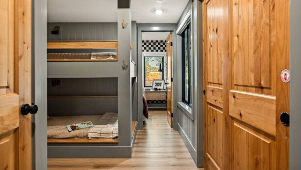 A narrow hallway with bunk beds on one side and wooden doors on the other. - Slope & Cedar House | Hot tub, Steps 2 Snow Summit (Big Bear Lake)