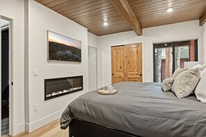 A bedroom with a bed, a fireplace, a wooden door, and a window. - Slope & Cedar House | Hot tub, Steps 2 Snow Summit (Big Bear Lake)