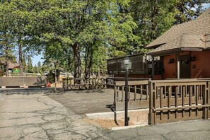 A parking area with a paved surface, a wooden fence, and a building with a brown roof. - Slope & Cedar House | Hot tub, Steps 2 Snow Summit (Big Bear Lake)