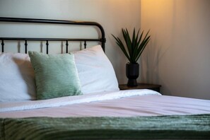 A neatly made bed with a green pillow and a white pillow, a black metal headboard, and a potted plant on a bedside table. - Modern Tiny Home! Walk to Parkway*Hot Tub*Sleeps 6 (Pigeon Forge)