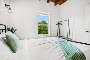 Een slaapkamer met een bed, een raam, een plant en een hanglamp.