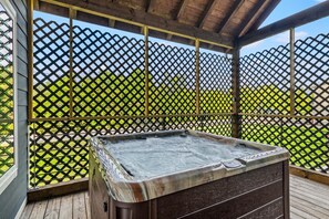 A hot tub in a covered outdoor area with a wooden deck and a lattice fence. - Modern Tiny Home! Walk to Parkway*Hot Tub*Sleeps 6 (Pigeon Forge)