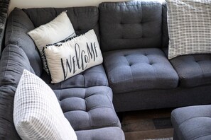 A sectional sofa with a 'WELCOME' pillow, a patterned pillow, and a striped pillow. - Modern Tiny Home! Walk to Parkway*Hot Tub*Sleeps 6 (Pigeon Forge)