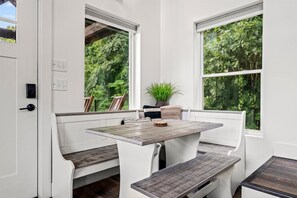 A room with a table and benches, large windows with a view of greenery, and a potted plant. - Modern Tiny Home! Walk to Parkway*Hot Tub*Sleeps 6 (Pigeon Forge)