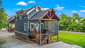A two-story house with a covered porch and a small deck. - Modern Tiny Home! Walk to Parkway*Hot Tub*Sleeps 6 (Pigeon Forge)